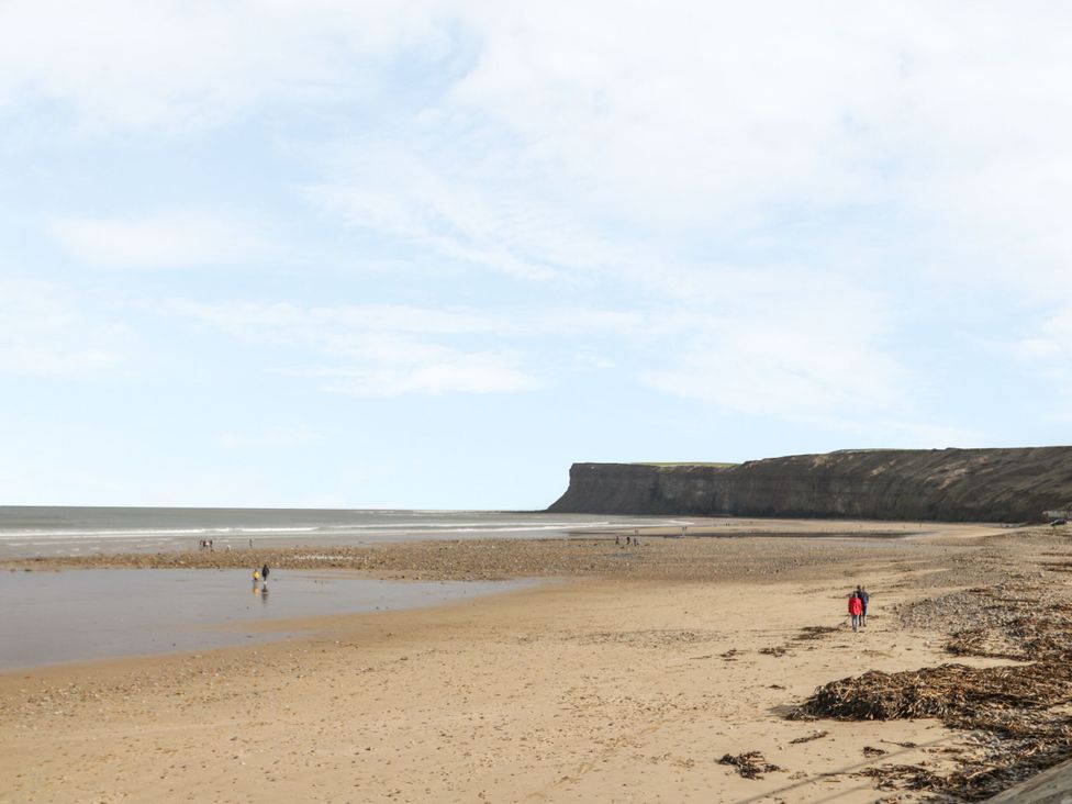 A beach scene with cliffs and people walking at The Cow Byre Lingdale near Saltburn-by-the-Sea