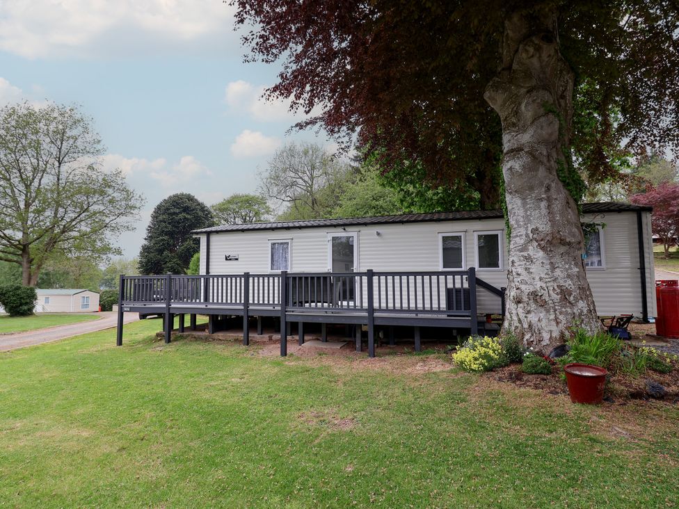 A static caravan with a decking area surrounded by grass and trees at Willerby Malton in Ruthin