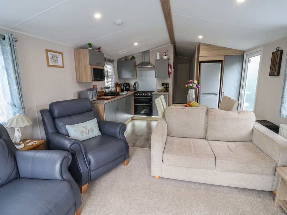 A living room with a sofa, armchair and kitchen area at Willerby Malton in Ruthin