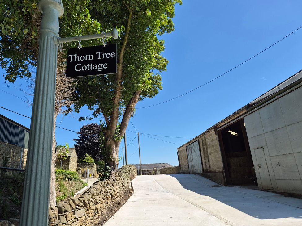 A sign for Thorn Tree Cottage with farm buildings and trees at Thorn Tree Cottage in Aston near Hope