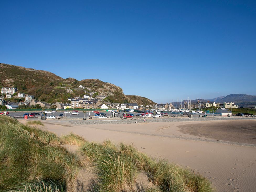 A beach with cars parked and houses on a hillside at Harbour Cottage Barmouth