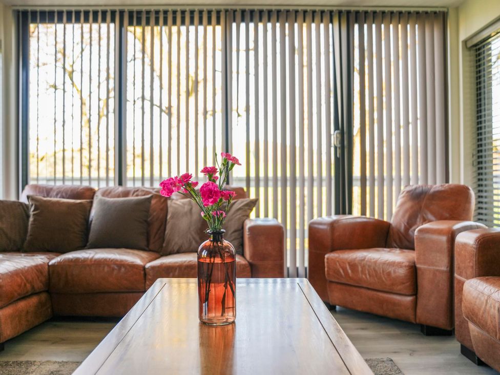 A living room with a sofa and armchairs with a vase of flowers at Oak Lodge in Llangunllo