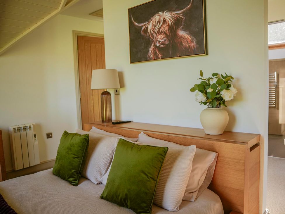 A bedroom featuring a bed, lamp, painting, and vase with flowers at Oak Lodge in Llangunllo