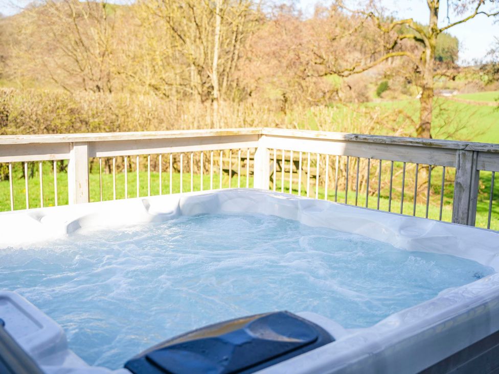 A hot tub on a wooden deck with trees in the background at Oak Lodge in Llangunllo