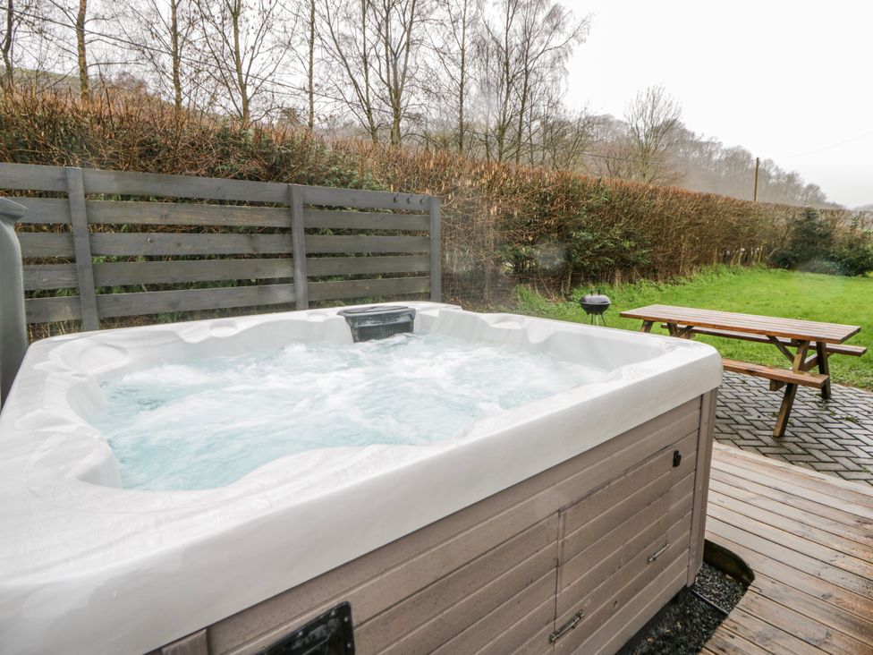 A hot tub with a wooden bench and lawn at Willow Lodge in Knighton