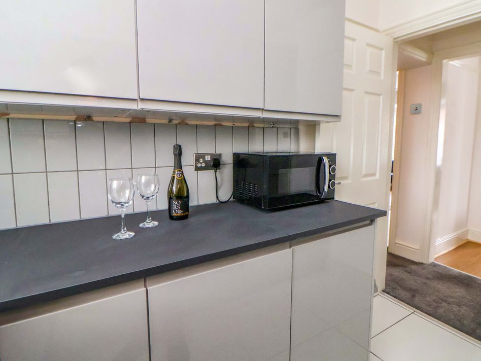 A kitchen with a microwave, wine glasses, and a bottle of wine at Wallasey Village Escape by the Sea, Wallasey