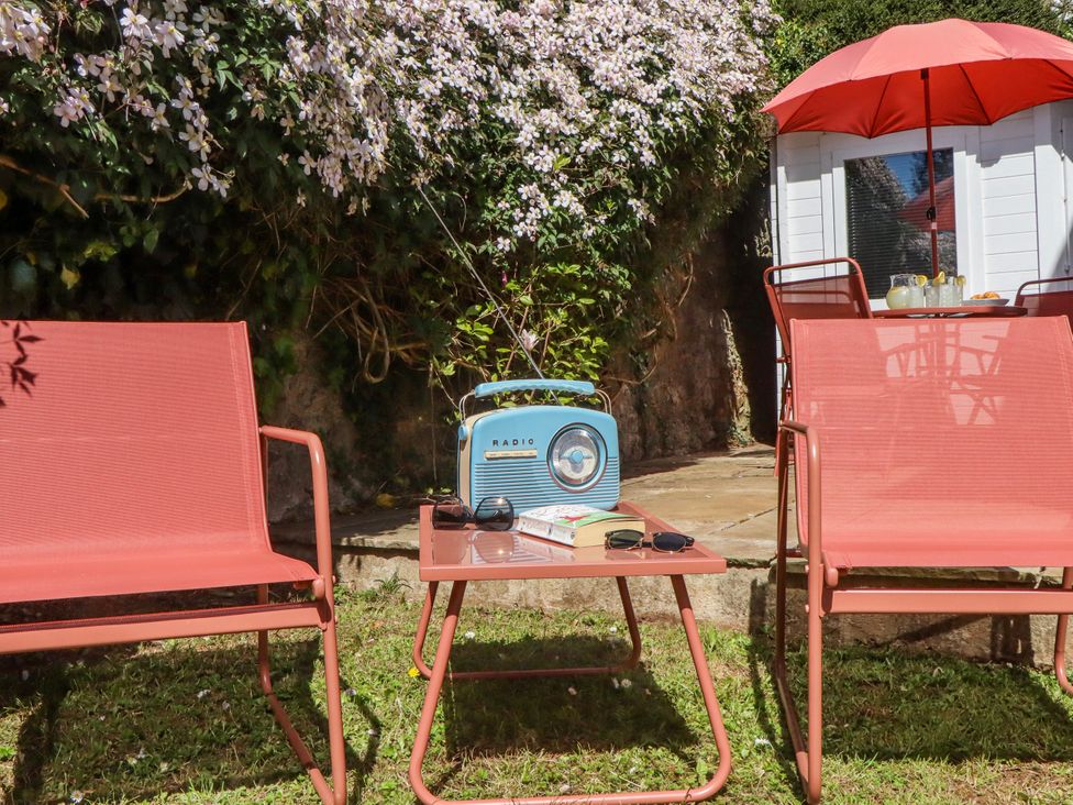 A garden with chairs, a table, a radio and a book at The Arches in Torquay
