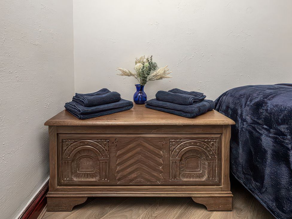 A wooden chest with folded towels and a vase with flowers in a bedroom at Preswylfa