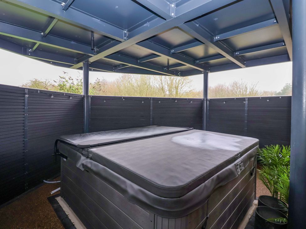 A hot tub under a roof structure in an outdoor area at Swing Bridge Cottage