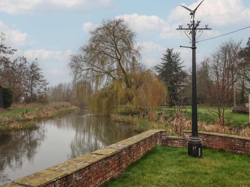 A river with a brick wall and weather vane at Mill Race Cottage in Driffield