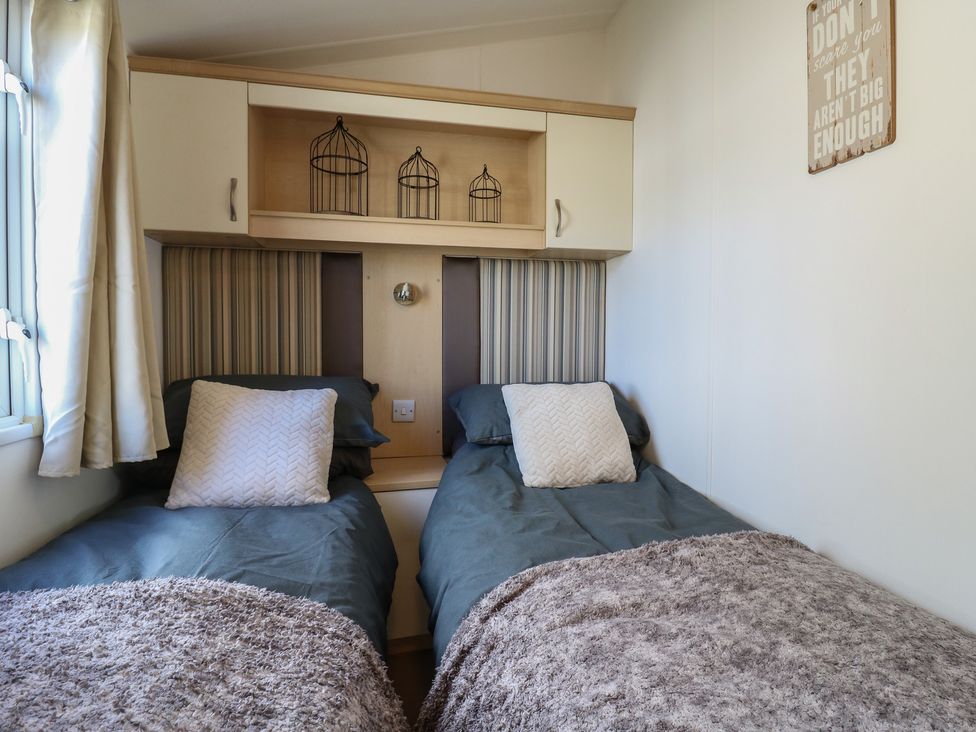 A bedroom with two single beds and a shelf with decorative items at 2 bed Caravan Stowmarket