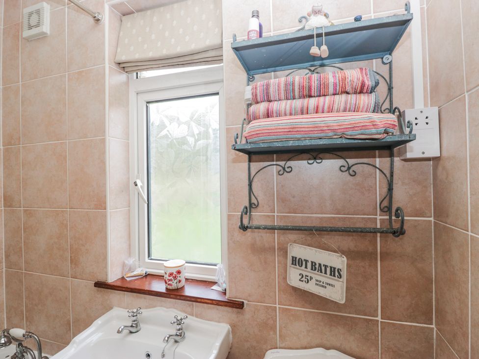 A bathroom with towels on a shelf and a bathtub at Linden Lea in Field Broughton near Cartmel