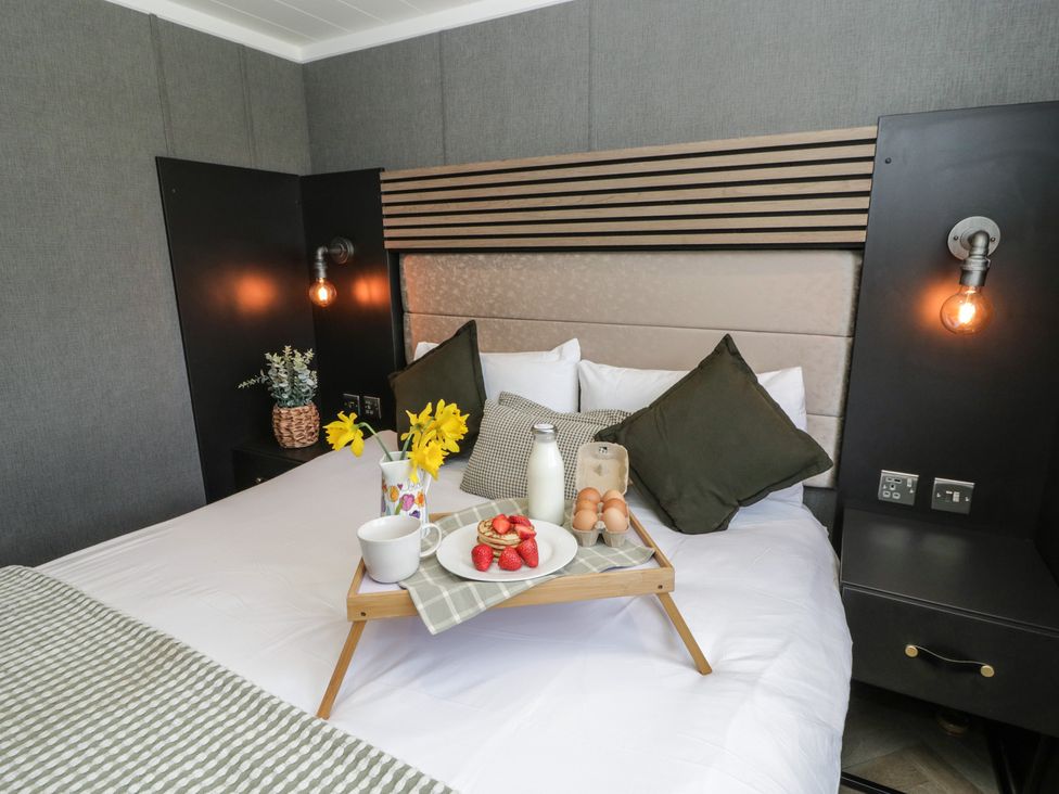 A bedroom with a bed, bedside table, light fixture and a tray of food at Daverneithon 3 near Llandrindod Wells