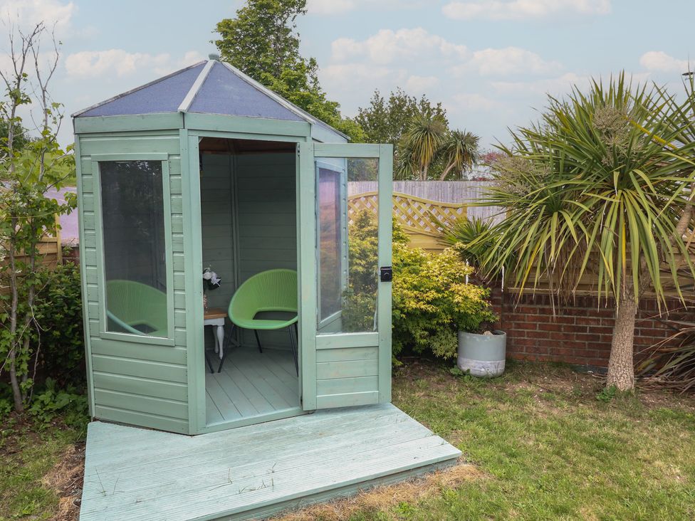 A garden shed with two green chairs and a table at The Coach House Near Charminster