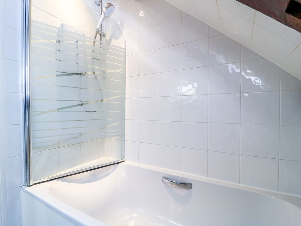A bathtub with a shower and tiles at The Coach House Near Charminster