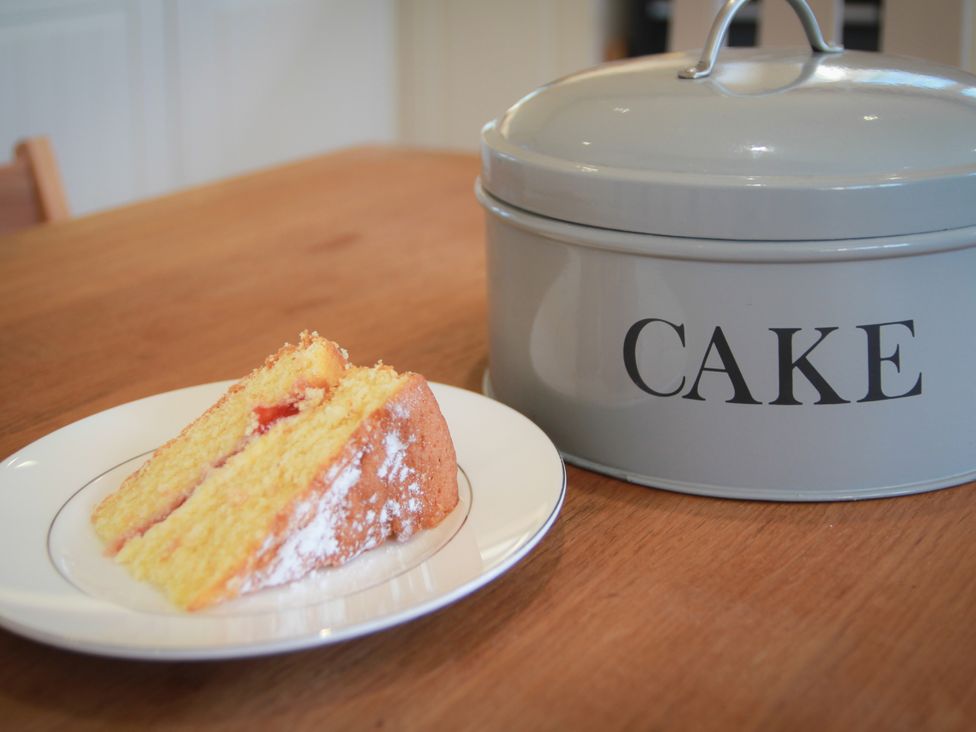 A slice of cake on a plate next to a cake tin at Stanbridge Cottage in Malmesbury
