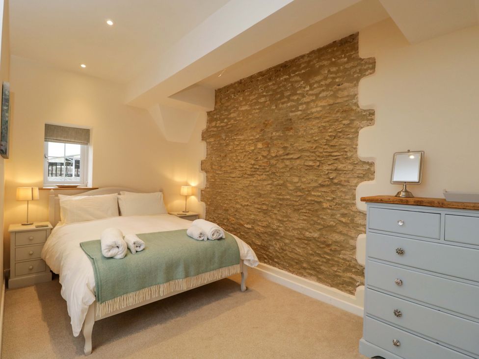 A bedroom with a bed, nightstands, and a stone wall at Stanbridge Cottage in Malmesbury