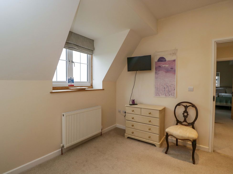 A bedroom with a window, radiator, television, chest of drawers and chair at Stanbridge Cottage in Malmesbury