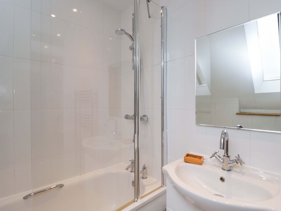 A bathroom featuring a bathtub with shower, sink, and a mirror at Stanbridge Cottage in Malmesbury