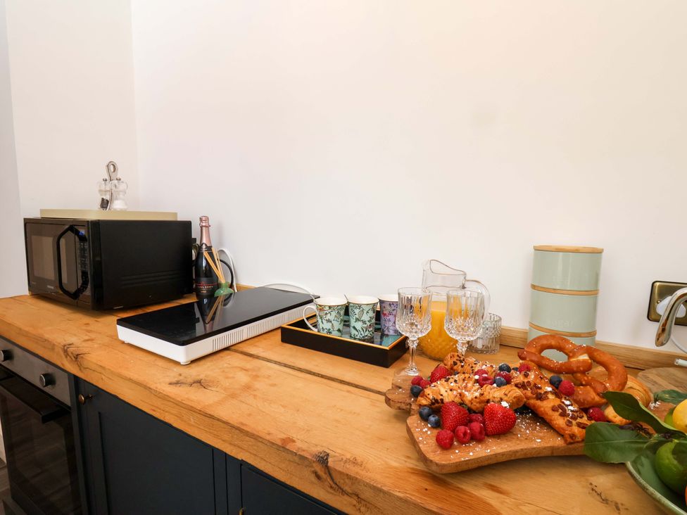 A kitchen counter with a microwave, pastries, fruit, and drinks at Hawthorn Lodge in Whitby