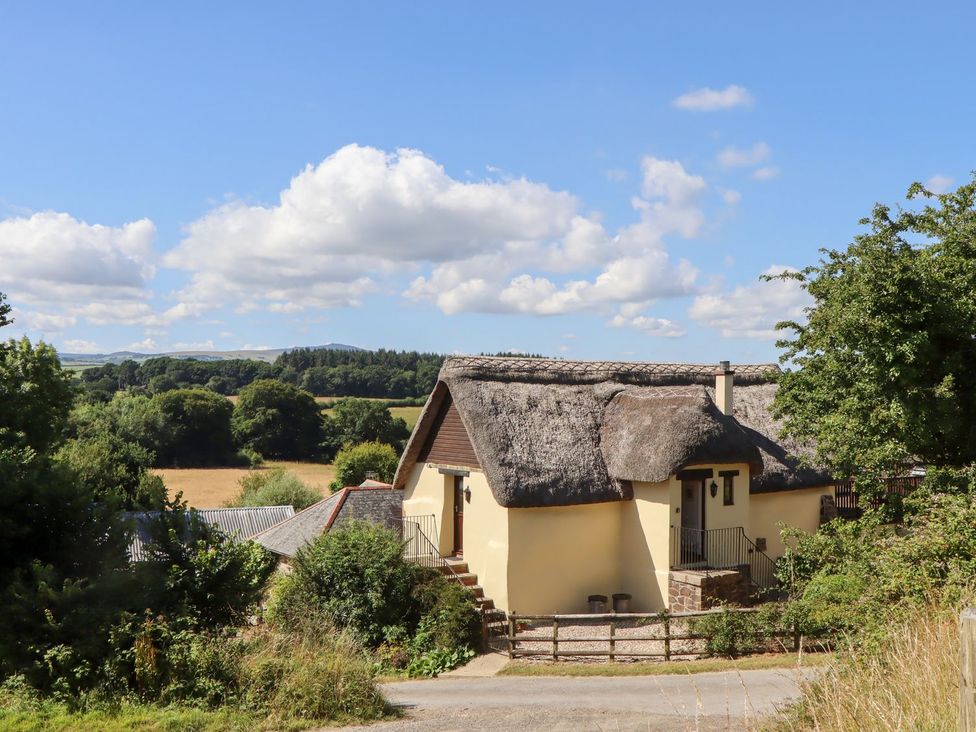 A house with a thatched roof and stairs surrounded by trees and fields at The Cottage in Sampford Courtenay