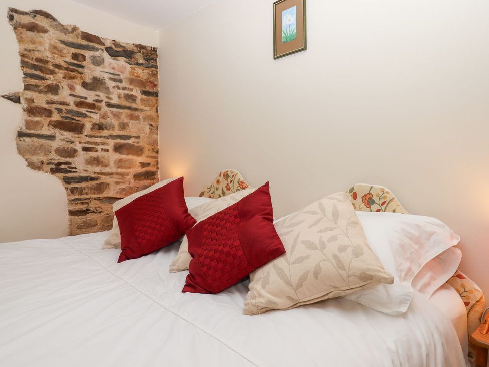A bedroom with a bed and a stone wall at The Cottage in Sampford Courtenay