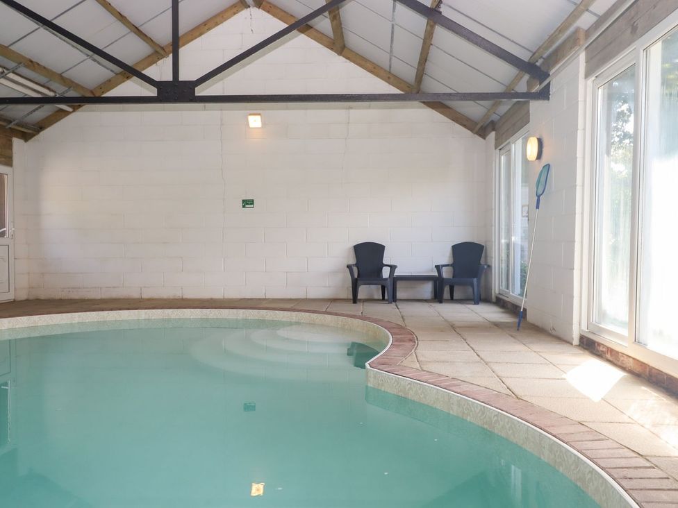 An indoor pool area with chairs and windows at The Cottage in Sampford Courtenay