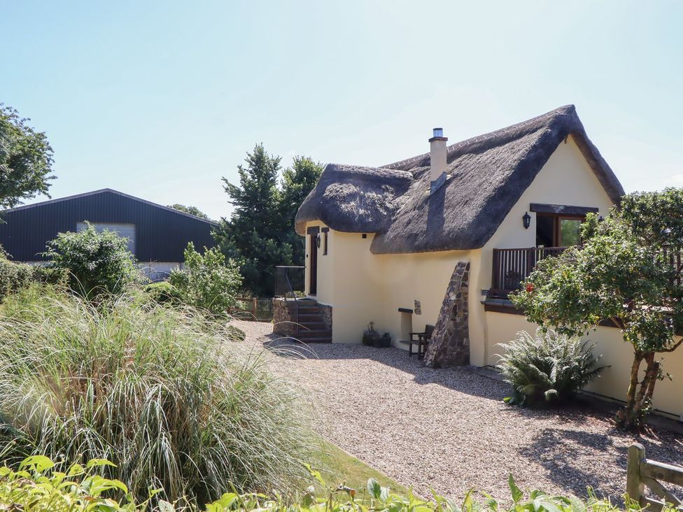 A house with a thatched roof and a garden at The Cottage in Sampford Courtenay