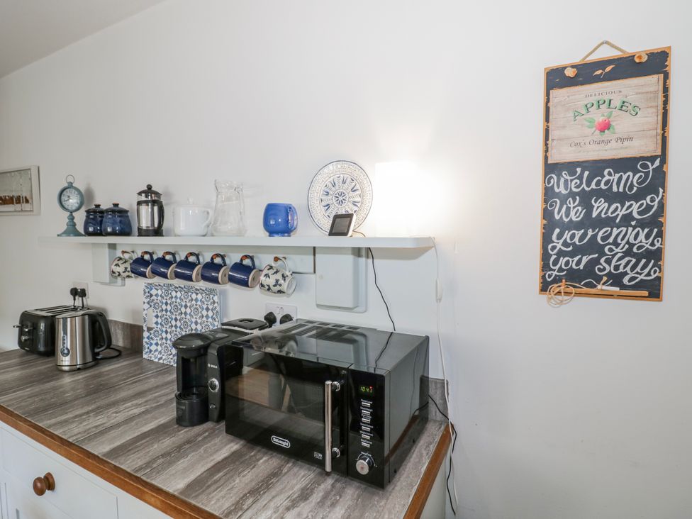A kitchen with appliances and a shelf displaying mugs at Halliday’s Cottages - The Folly, Greetham near Cottesmore