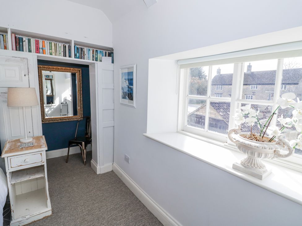 A bedroom with a bookshelf, lamp, and window at Halliday’s Cottages - The Folly near Greetham