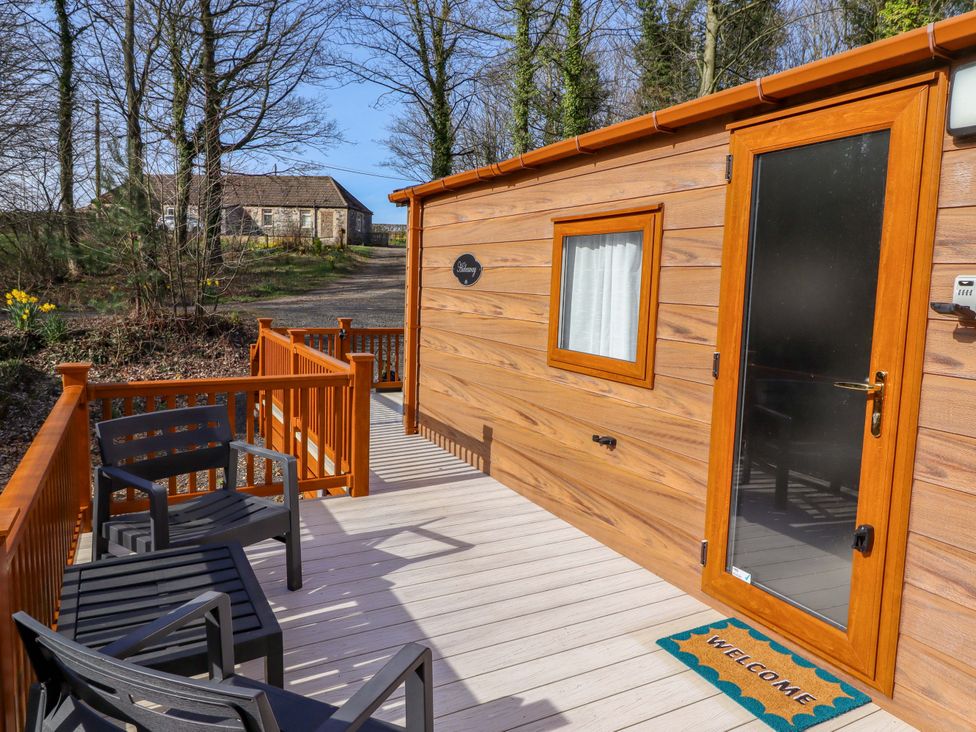 A wooden cabin with a welcome mat and outdoor seating in front at Gardeners Lodge 