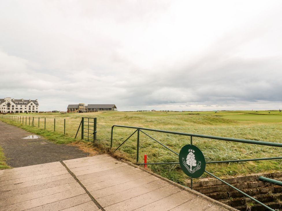 A golf course with a fence and buildings at Seaview Wellness Retreat in Carnoustie
