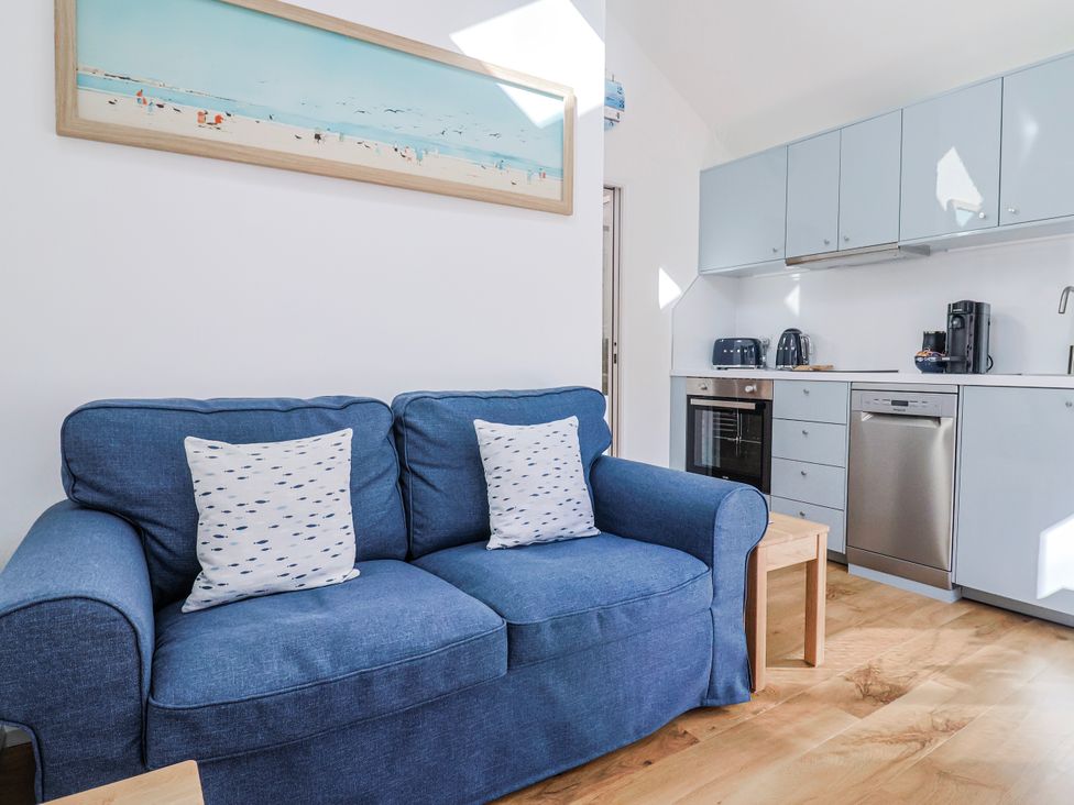 A living room with a blue sofa and kitchen cabinets at Le Petit Glen in Uplyme
