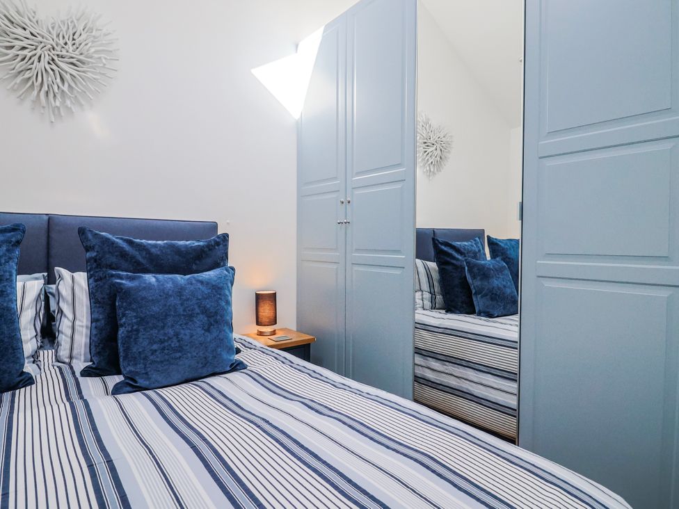 A bedroom with a bed, pillows, nightstand, and wardrobe at Le Petit Glen in Uplyme