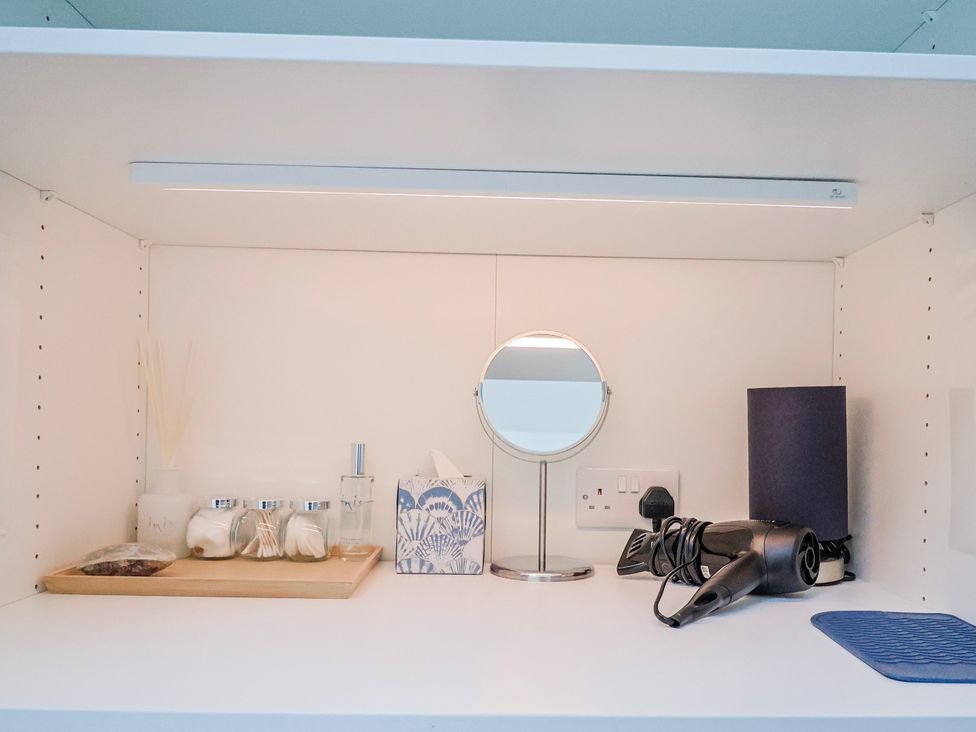 A bathroom shelf with a hair dryer and perfume bottle at Le Petit Glen in Uplyme