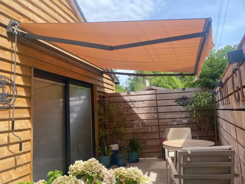 A garden area with an awning, table, and chair at Le Petit Glen in Uplyme