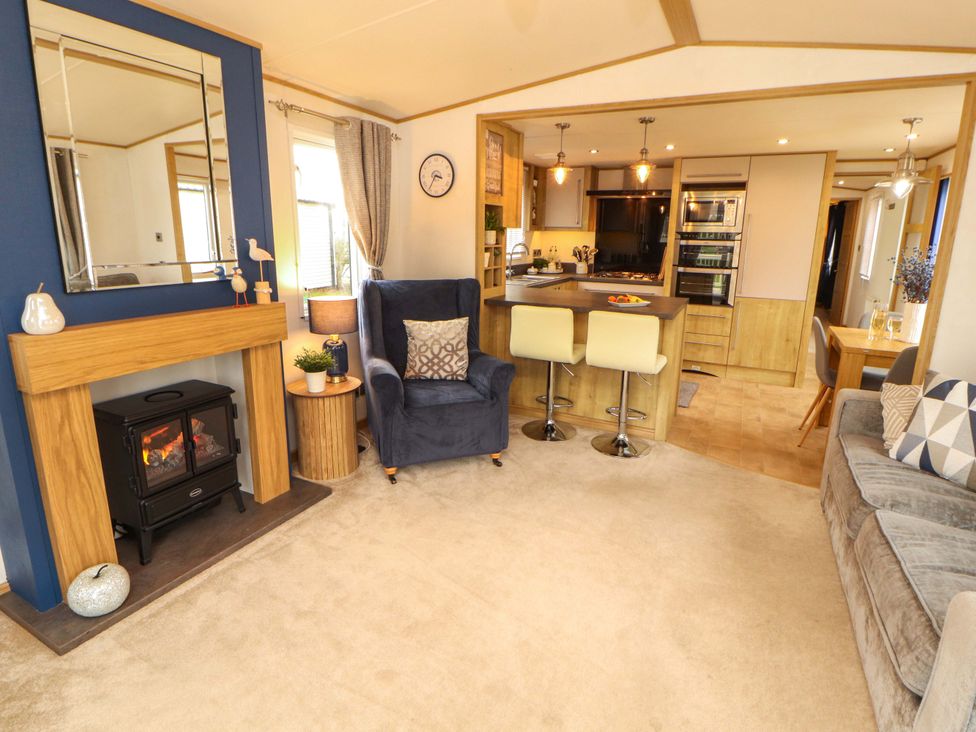 A living room with a fireplace and kitchen area at Hedgerow Lodge in Grange-Over-Sands