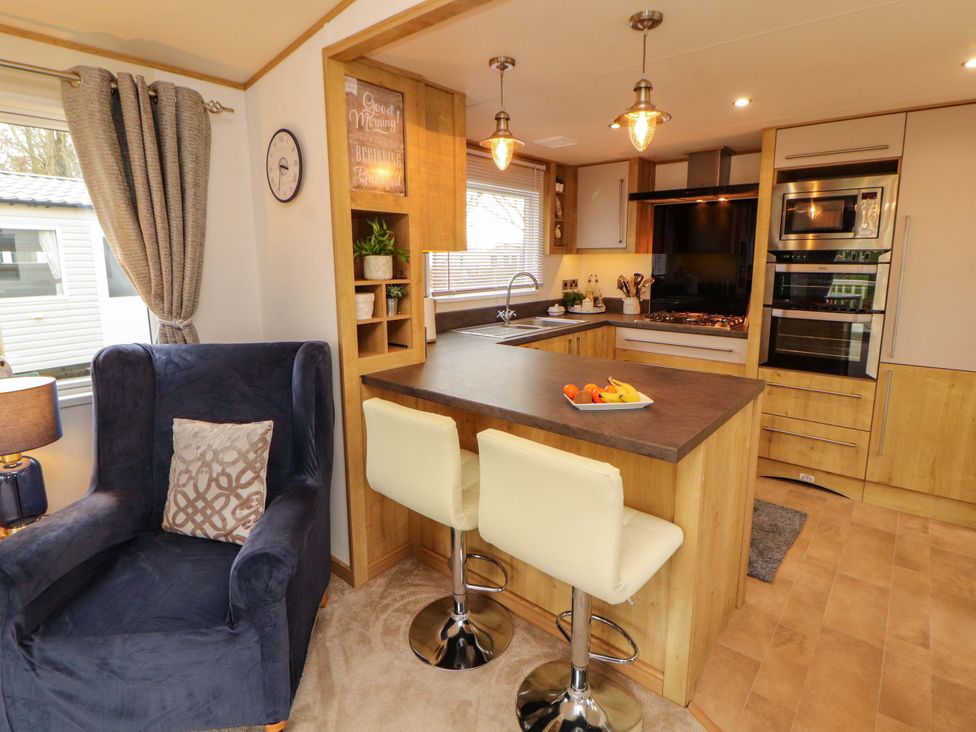 A kitchen with a table and bar stools at Hedgerow Lodge in Grange-Over-Sands