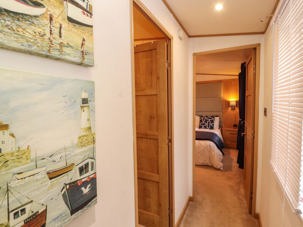 A hallway with paintings on the wall and doors leading to a bedroom at Hedgerow Lodge, Grange-Over-Sands