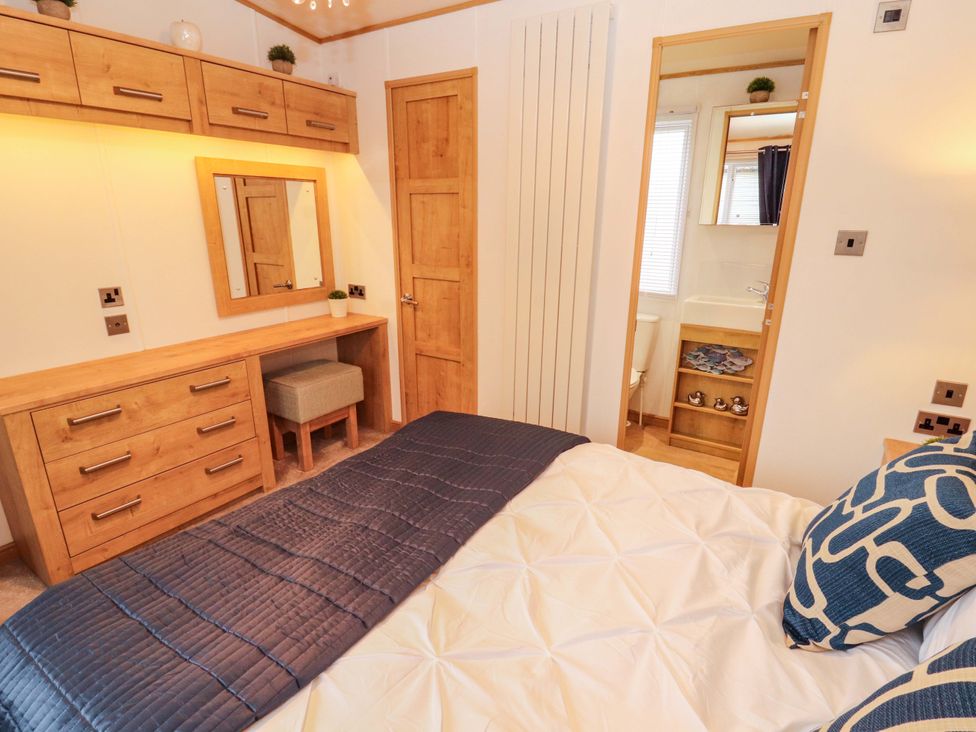 A bedroom featuring a bed, dresser, mirror, and bathroom entrance at Hedgerow Lodge in Grange-Over-Sands