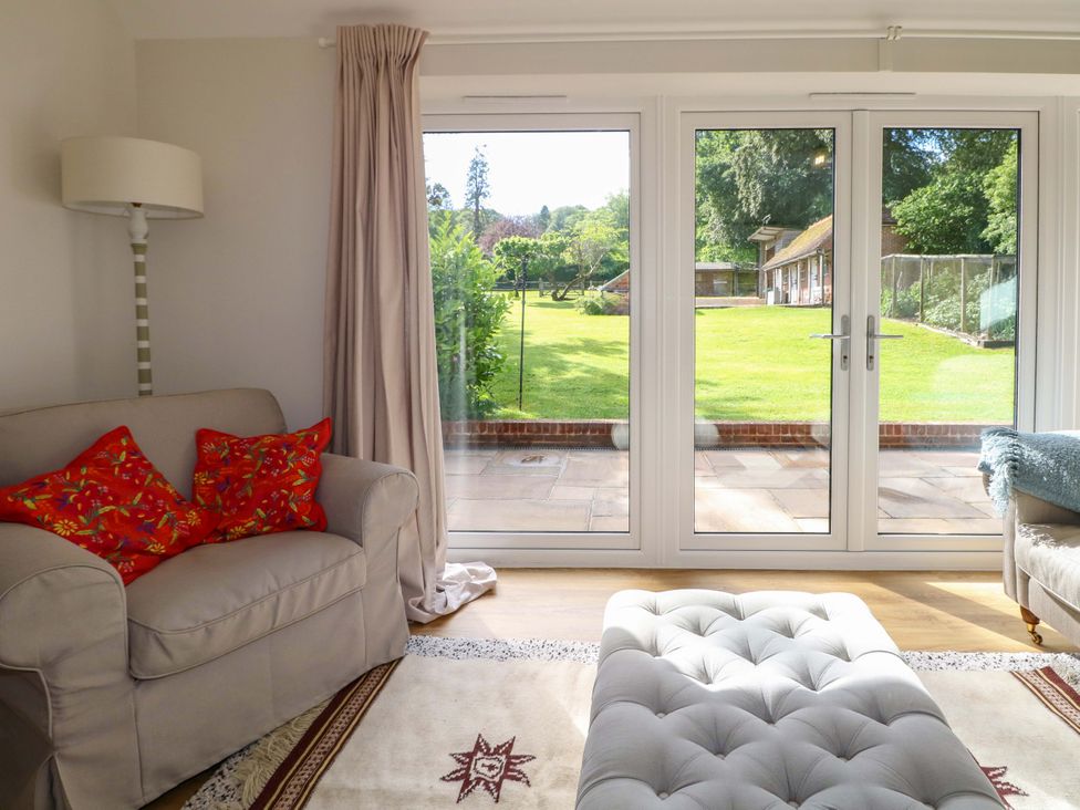 A living room with a view of the garden through sliding doors at Keepers Cottage in Petersfield