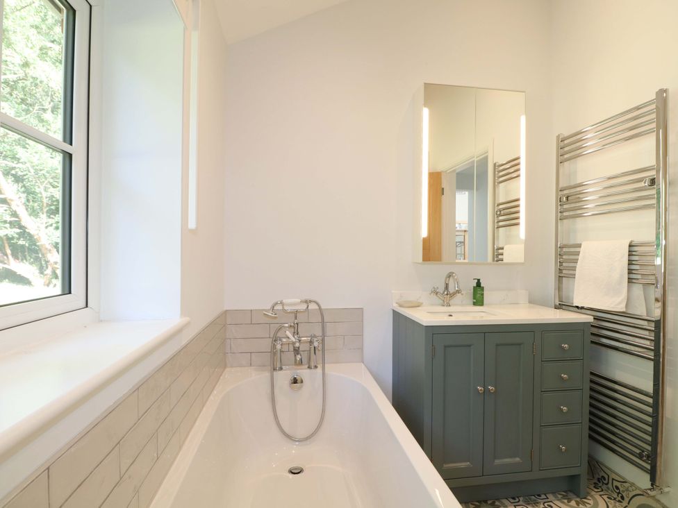 A bathroom with a bathtub and mirror at Keepers Cottage in Petersfield