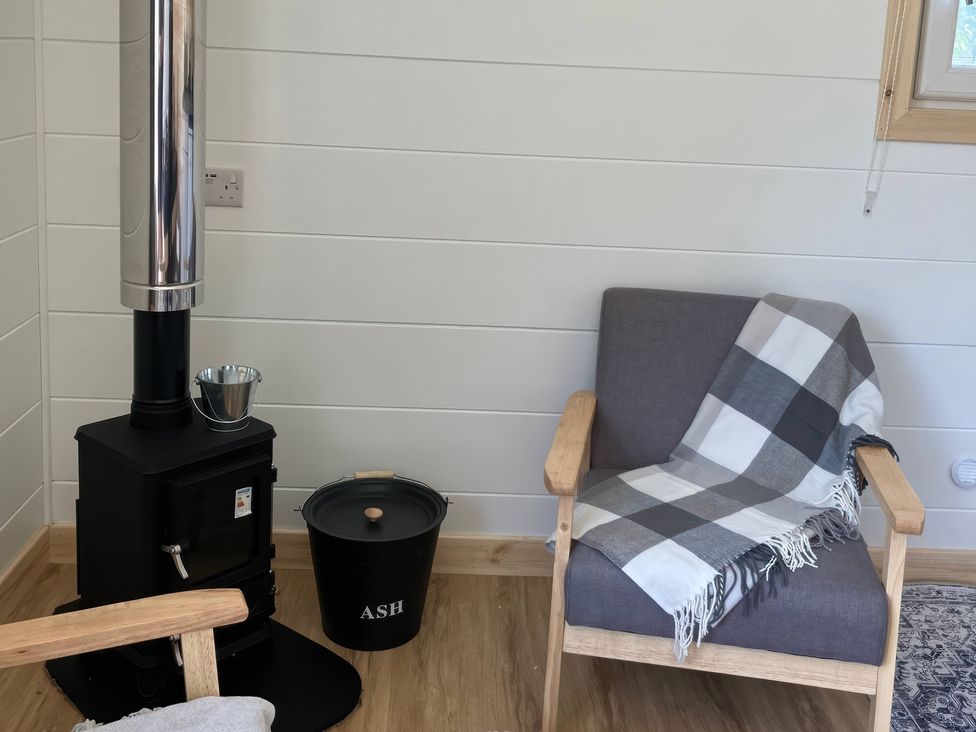 A snug with a stove, chair, blanket and bucket at Sherwood - Cosy Pod 4, Mansfield