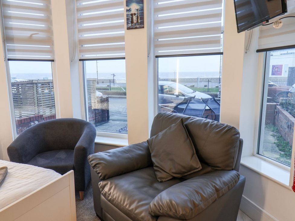 A living room with a sofa and armchair by windows at Frankie’s Seaview 1 in Bridlington