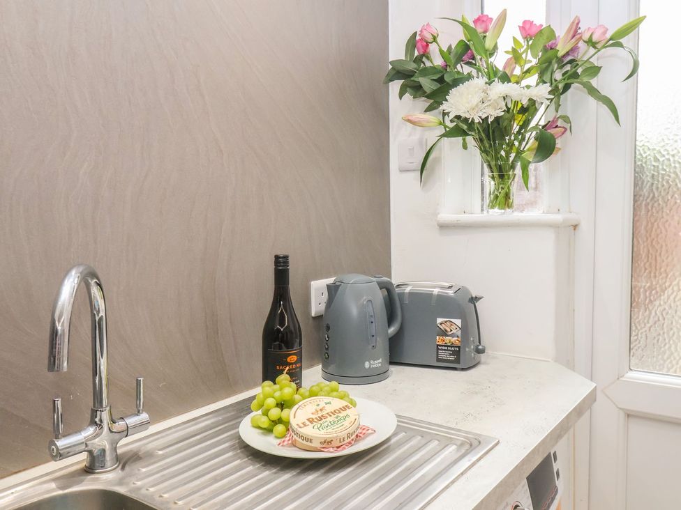 A kitchen with a sink, kettle, toaster, grapes, bottle, and flowers at Frankie’s Seaview 2 in Bridlington