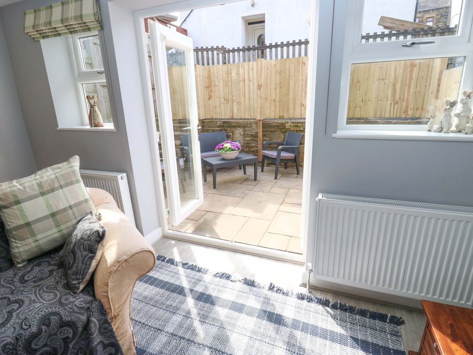 A living room with a sofa and doors leading to a patio at Milburn Cottage in Keighley