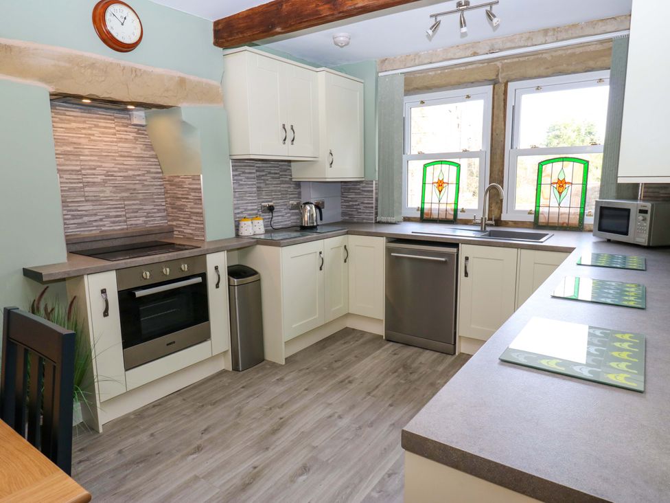 A kitchen with cabinets, oven, and stained glass windows at Milburn Cottage in Keighley