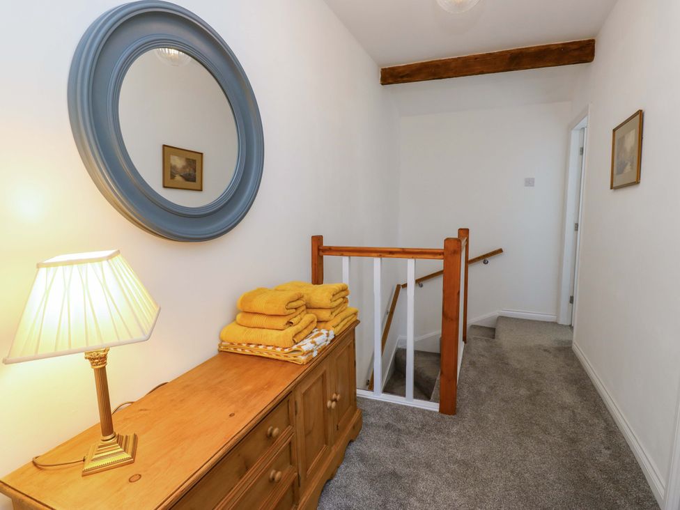 A hallway with a lamp and towels on a dresser at Milburn Cottage in Keighley