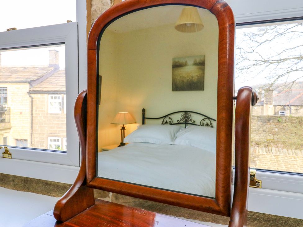 A mirror reflecting a bed with a lamp in a bedroom at Milburn Cottage in Keighley