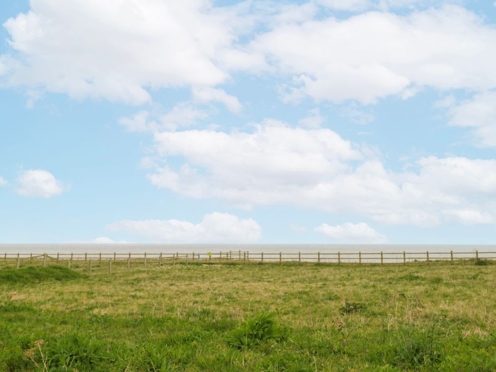 A grassy field with a fence and clouds at 59 Cliff Field in Lowestoft